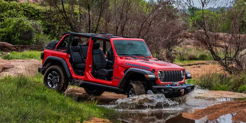 Jeep Wrangler in red color in mid of forest showcasing its unique design.