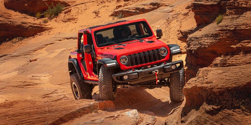 Red Jeep Wrangler Rubicon navigating rocky desert terrain.